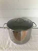 Stock pot exterior front view with glass lid on top, reflective polished surface, two side handles