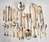 All silver plated silverware arranged on a white background showing various spoons, forks, tongs, and a candle snuffer.
