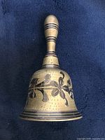 Side view of vintage brass bell showing floral etched pattern and handle with etched bands.