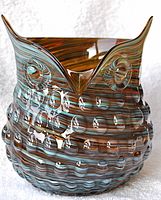 Front view of the owl-shaped glass pitcher showing the beige and blue swirl pattern and raised oval feather detail.