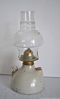 Full view of vintage oil lamp with clear glass chimney and pottery base.