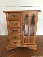 Front view of closed wooden jewelry box with five drawers and a glass-paneled door.