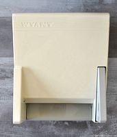 Front view of beige Wyant hand paper dispenser with visible top press latch and paper dispensing slot with serrated tear-off edge.