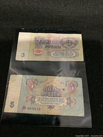 3 and 5 Russian Rubles banknotes from 1961 placed inside protective plastic sheet photographed against a black background.