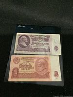 Photo showing both the 1961 Soviet 10 and 25 ruble banknotes placed on black fabric inside a protective sleeve.