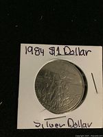 Front side of 1984 Canadian silver dollar coin showing Jacques Cartier design, in white protective holder with handwritten note.