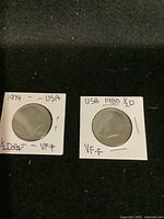 Two USA half dollar coins, one dated 1974 and the other 1980, mounted in protective holders.