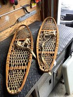 Pair of 36-inch vintage wooden snowshoes on metal surface with pegboard wall background.