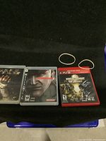Three PS3 game cases laid side by side showing front cover art: Dead Space, Metal Gear Solid 4, Mortal Kombat vs. DC Universe