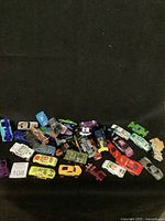 Wide view of 38 different toy cars in multiple colors and styles arranged on dark background.