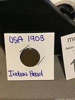 1903 American Indian Head penny displayed in white cardboard holder labeled with handwritten date and type.