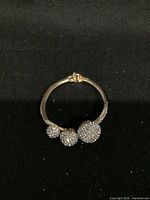 Top-down photo of the bracelet showing three crystal-encrusted spherical balls on a metal band against a black background.