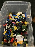 Top-down view of a clear plastic storage bin filled with a variety of colorful Lego and other building blocks in assorted shapes and sizes.