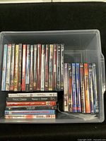 Top-down view inside plastic bin showing 30 DVDs, reveals spines and some titles like Da Vinci Code, Wolverine, Doom, Hitch, and others
