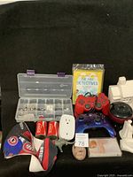 Overview of lot items showing controllers, plastic houses, book, charm container, Coke cans, Montreal hat, and other small items