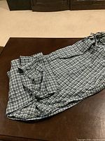 Long plaid pajama pants with elastic waistband and drawstring, laid out on table