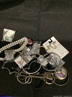 Overview of assorted costume jewelry including bracelets, earrings, necklaces, and pocket watch pendant on black background