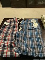 Two pairs of plaid pajama shorts laid flat on a table showing tags and different plaid patterns in red/navy and blue/navy color schemes.