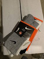 Three pairs of Nike men's socks including gray, white, and black. Packaged with Nike branded moisture-wicking label.