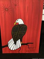 Full view of the original eagle painting on red background, showing the stylized bald eagle perched on a branch and the two star-like designs in the background.