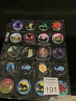 Plastic page holding 20 assorted colorful pogs in clear sleeves with various designs including animals, cartoon characters, and brand logos.