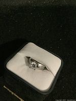 Ring in jewelry box showing clear single center stone and silver band.