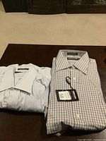 Photo showing two Kirkland brand men's dress shirts folded and placed on a table, one blue and white striped, the other blue and white checkered.