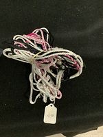Pile of various woven dog and cat leashes in white, pink, and black on a black background.