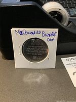 Front side of the McDonald's breakfast promotional coin in white cardboard holder with handwritten note