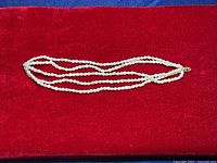 Full view of the three-strand rice pearl necklace displayed on red velvet background.