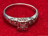 Front view of ring on red background showing square cluster setting with central and corner diamonds