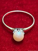 Close-up front view of the ring showing the white pearl and gold band on red background