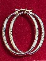 Pair of oval hoop earrings displayed flat on red fabric background