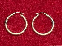 Pair of yellow and white gold hoop earrings on red background showing overall appearance