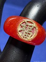 Close-up of 14k yellow gold Asian lucky symbol carved into circular inset on smooth red carnelian ring band.