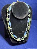 Turquoise and blue agate gemstone necklaces displayed on a black neck stand against a blue background.