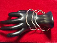 Three sterling silver wavy bangles displayed on black hand jewelry display on red background.