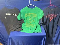 Three band T-shirts hanging on hangers, Metallica, Led Zeppelin, Van Halen designs