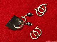 Three pairs of sterling silver earrings displayed on red background. One pair has dangling black onyx beads.