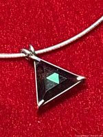 Close-up photo of the triangular pendant showing the green crystal and sterling silver frame on a red background.