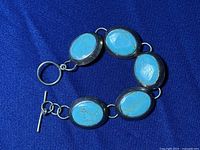 Turquoise bracelet laid flat on blue cloth showing the face with five oval turquoise stones set in sterling silver and toggle clasp on one end.