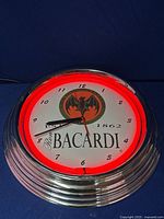 Lit Bacardi neon clock showing red neon illumination and time display, chrome rim, Bacardi logo.