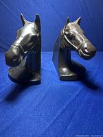 Front view of two bronze horse head bookends on blue background showing detailed horse faces and bases.