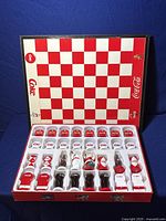 Opened chessboard showing Coca Cola themed red and white checkered board and 32 detailed chess pieces including polar bear, Santa Claus, and bottle designs.