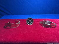 Front view of three jewelry items on red velvet background, showing leaf style cuff bracelet, round decorative ring, and hammered bracelet with carnelian.