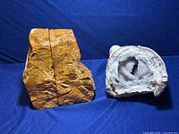 Two large petrified wood pieces standing upright as bookends next to a geode with exposed crystal cavity, all on a blue fabric background.