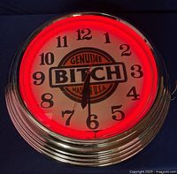 Front view of neon clock powered on, red neon ring glowing around white clock face with black numbers and central logo.