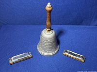 Full view of wood handle bell with two harmonicas placed on either side.