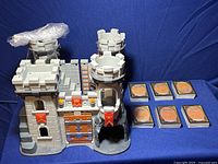 Photo of play castle with six visible stacks of Magic The Gathering cards beside it on a blue backdrop.