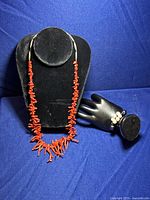 Red coral branch necklace on black display bust and white pearl & hematite bead bracelet on black hand display shown together